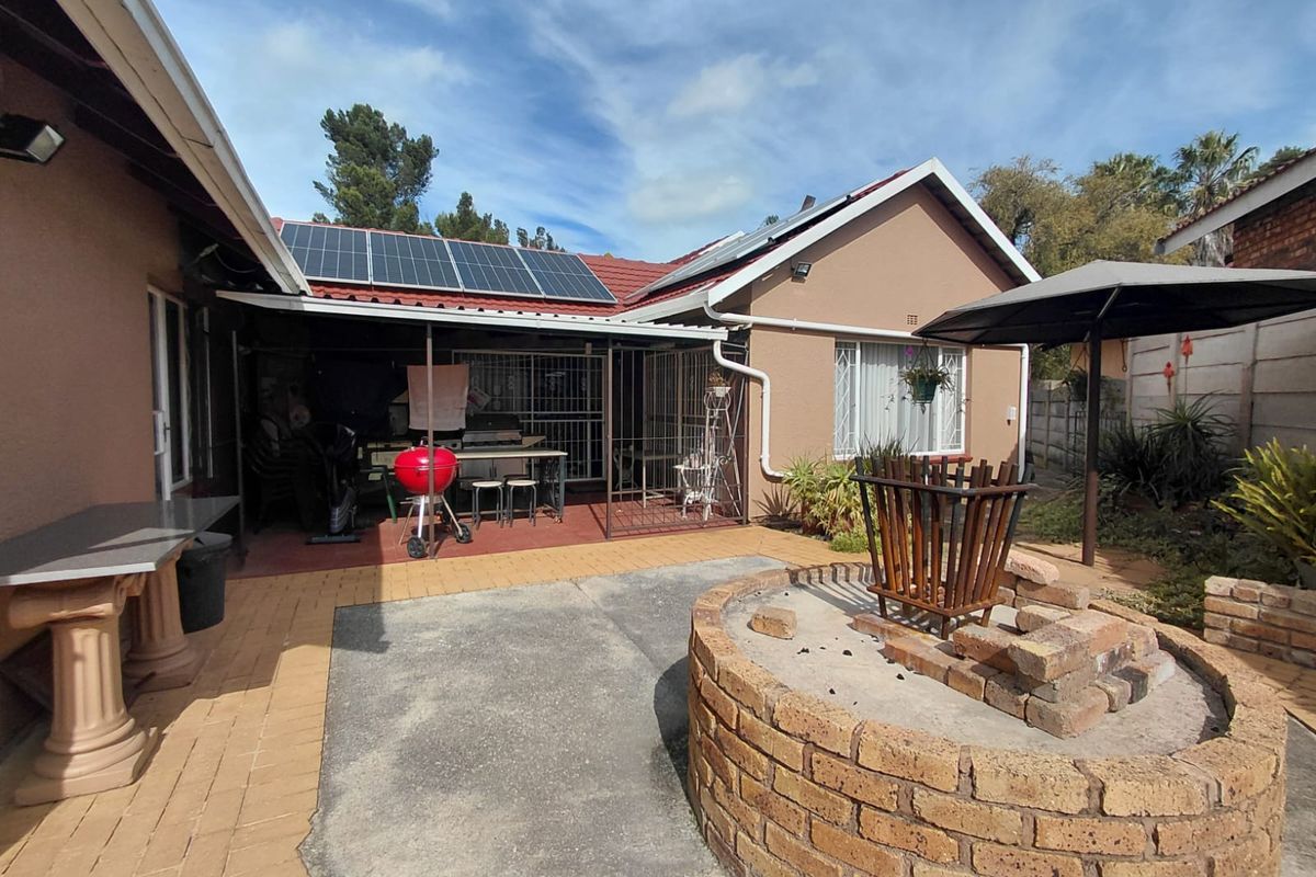 Rear outdoor entertainment area featuring a covered patio, built-in brick fire pit, and roof-mounted solar panels.