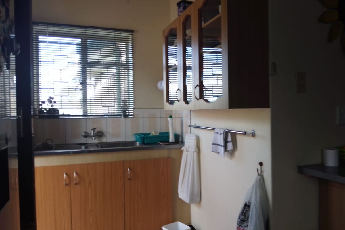 A functional kitchen area featuring wooden cabinetry, a stainless steel sink, and tiled splashbacks, providing a practical space for food preparation and cleaning.