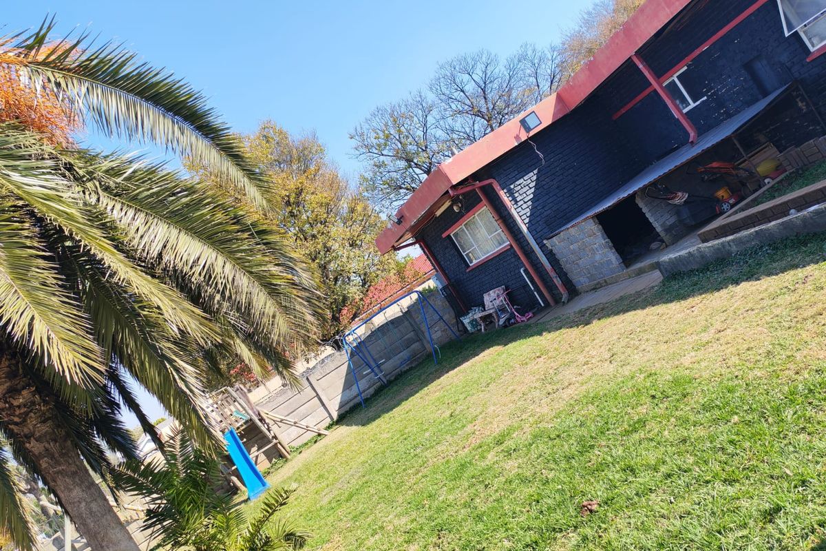Rear exterior view of the property featuring a lawn, covered patio area, and concrete boundary wall.