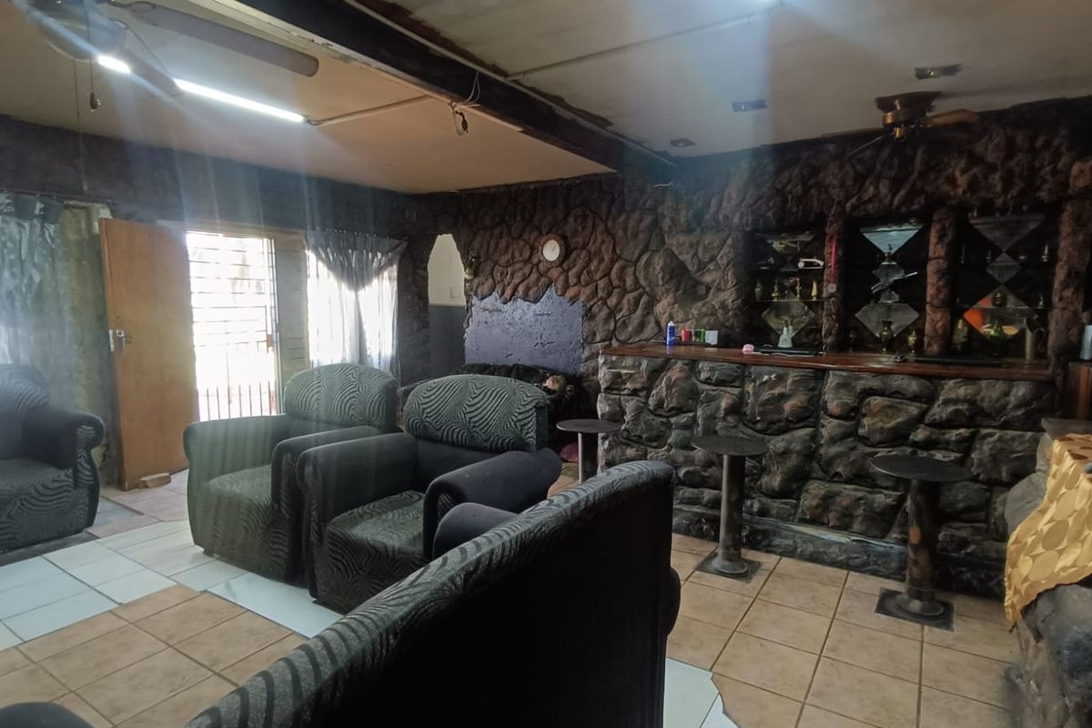 Living room featuring a prominent built-in stone bar, tiled flooring, and ceiling fan, offering a rustic aesthetic with potential for modernization.