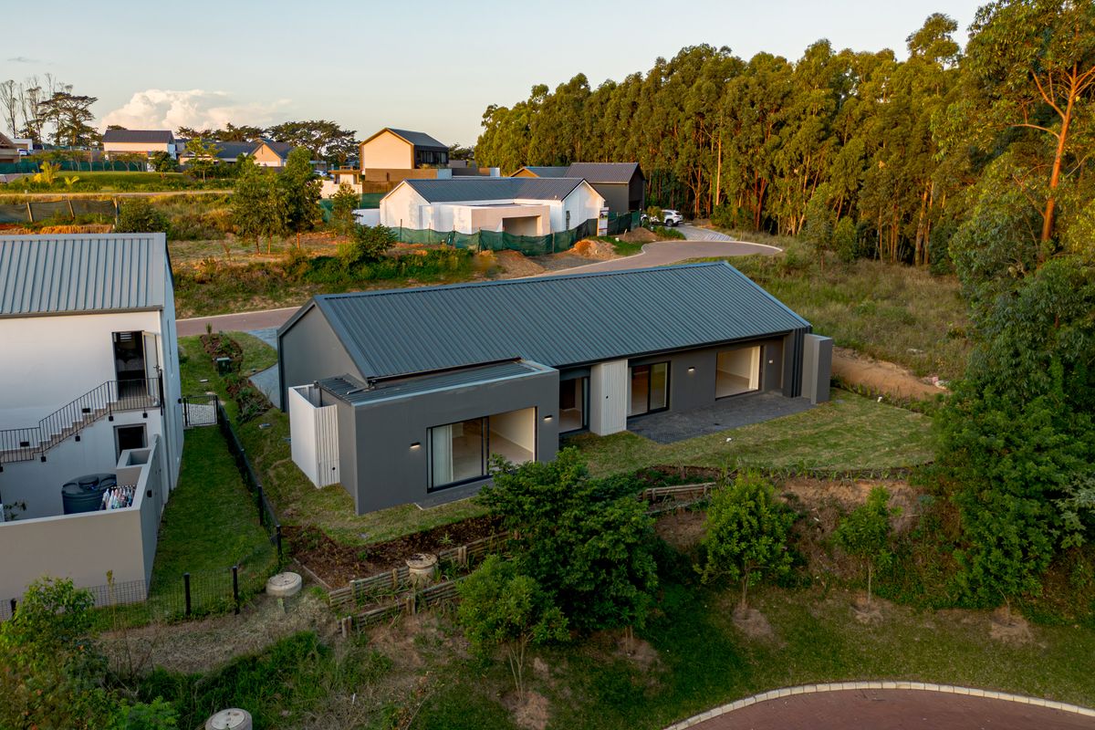 Aerial view of a modern single-story residence featuring a dark metal roof, grey exterior walls, and sliding glass doors opening onto a paved patio.