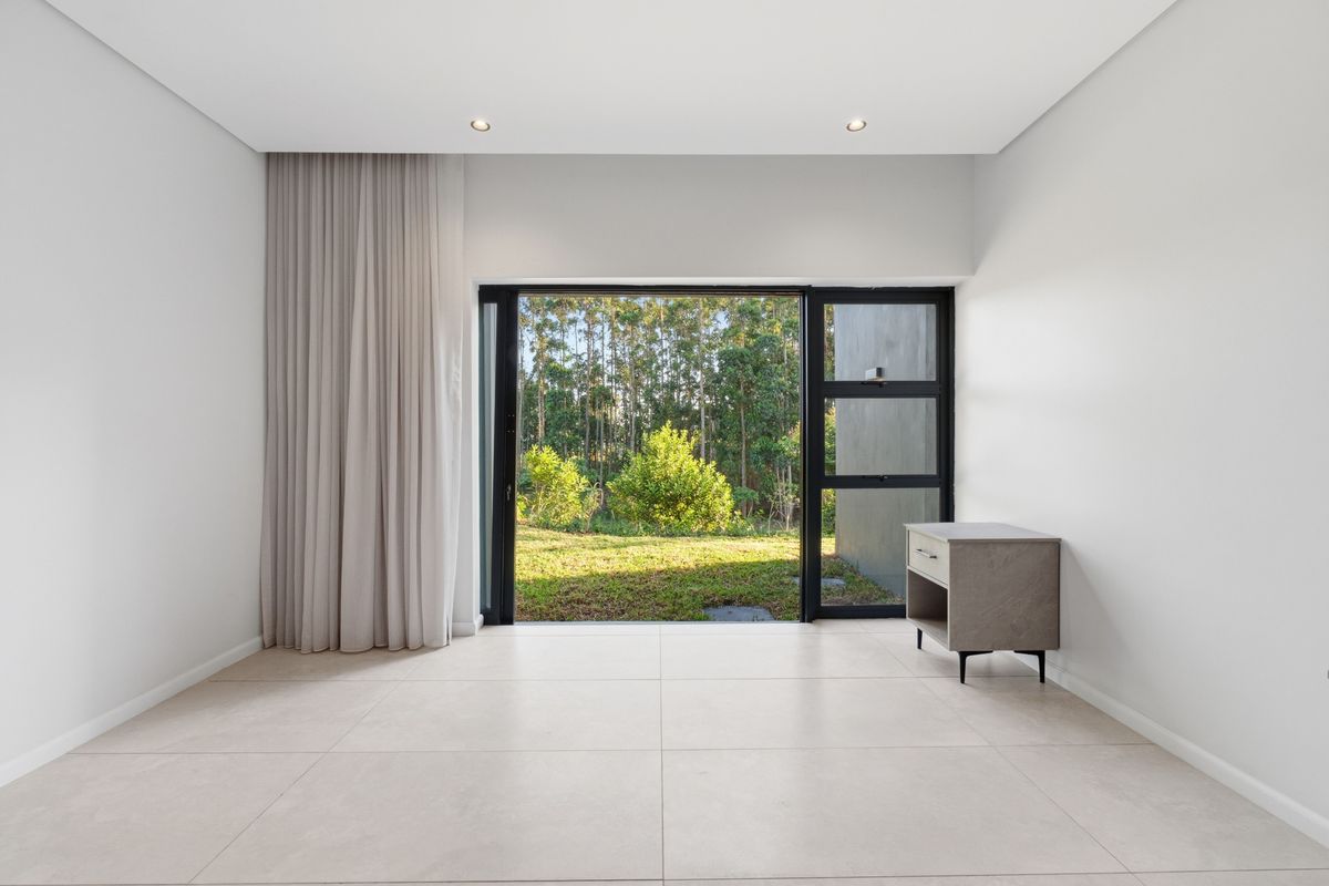 A bright, modern living space featuring large format floor tiles, recessed lighting, and a sliding glass door opening to a garden view.