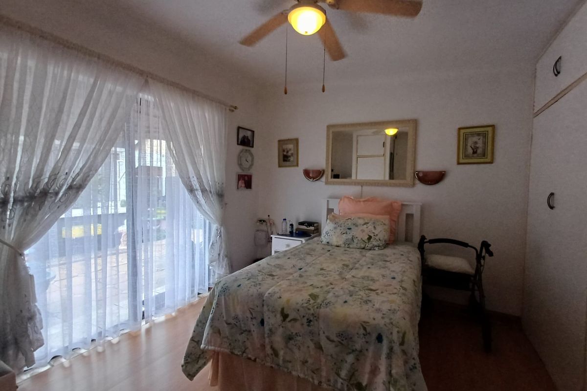 A well-lit bedroom featuring laminate flooring, built-in cupboards, a ceiling fan, and a sliding glass door providing access to the outdoor area.