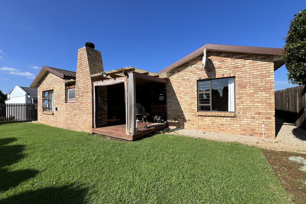 Rear view of the house featuring a brick facade, a chimney, and a covered timber patio area overlooking the lawn.
