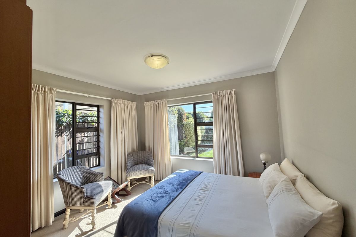 A well-lit bedroom featuring dual aspect windows with security bars, neutral wall tones, and carpeted flooring.