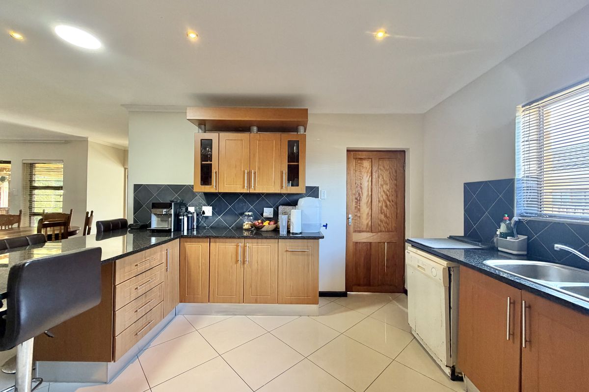 A functional kitchen featuring wooden cabinetry, dark granite countertops, tiled backsplash, and integrated sink, with an adjacent breakfast bar area.