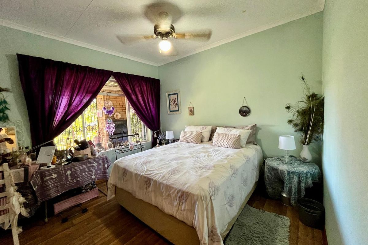 A bedroom featuring light green walls, wood-look flooring, and a ceiling fan, with natural light entering through a window with security bars.
