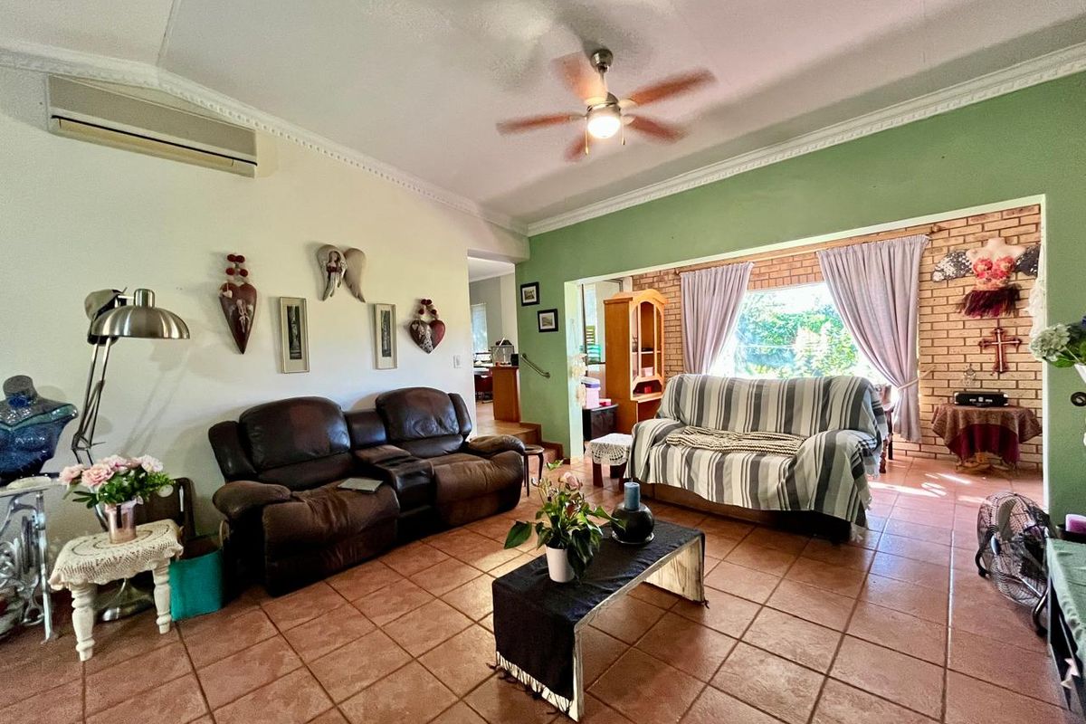 Spacious living area featuring terracotta floor tiles, a ceiling fan, and an exposed brick feature wall with natural light.