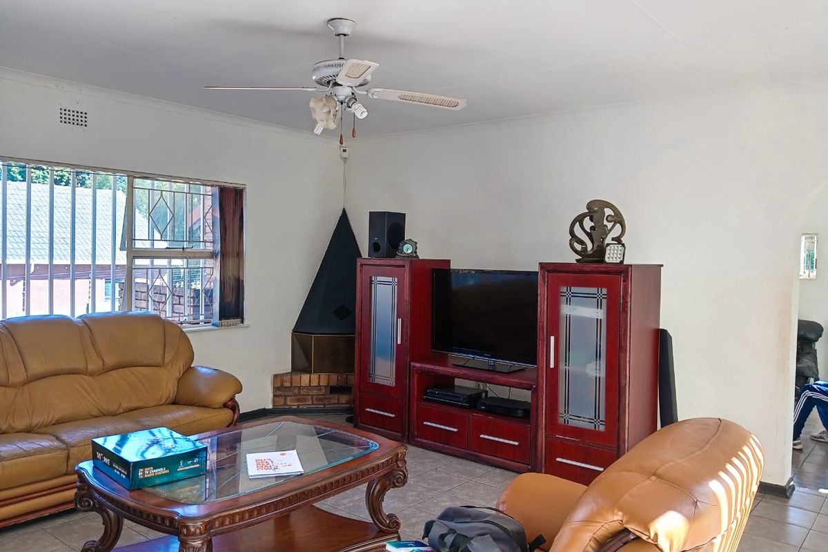 A living room featuring a corner fireplace, ceiling fan, and tiled flooring, with security bars installed on the windows.
