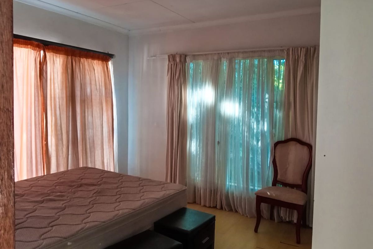 A bedroom featuring laminate flooring and large windows with curtains, offering a neutral space ready for personalization.