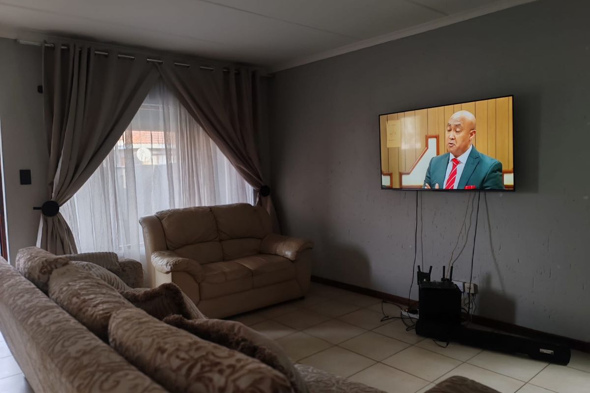 A living room featuring tiled flooring, a wall-mounted television, and large window with curtain treatments.