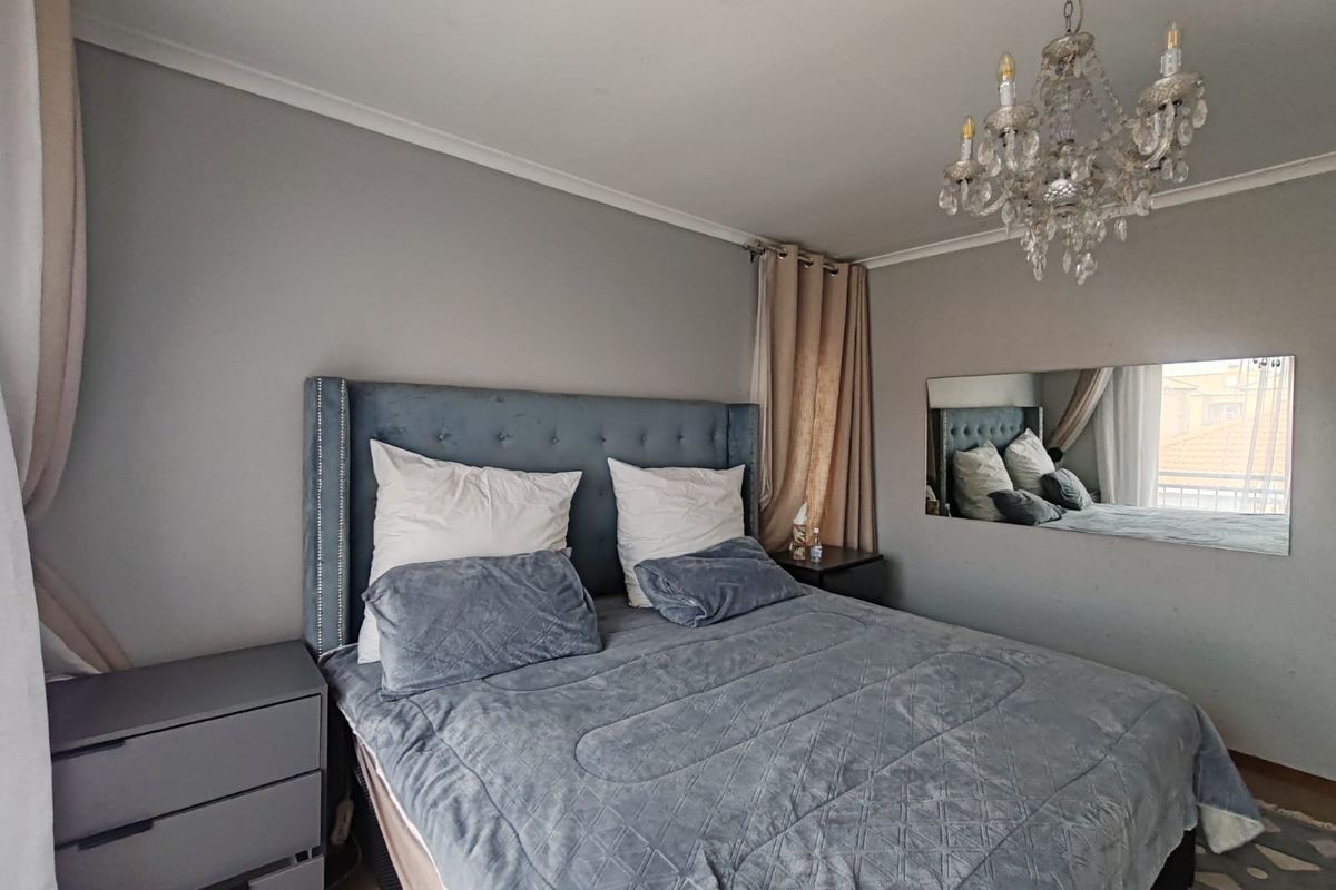 A well-maintained bedroom featuring a decorative crystal chandelier, crown molding, and a large wall-mounted mirror, providing a bright and comfortable living space.