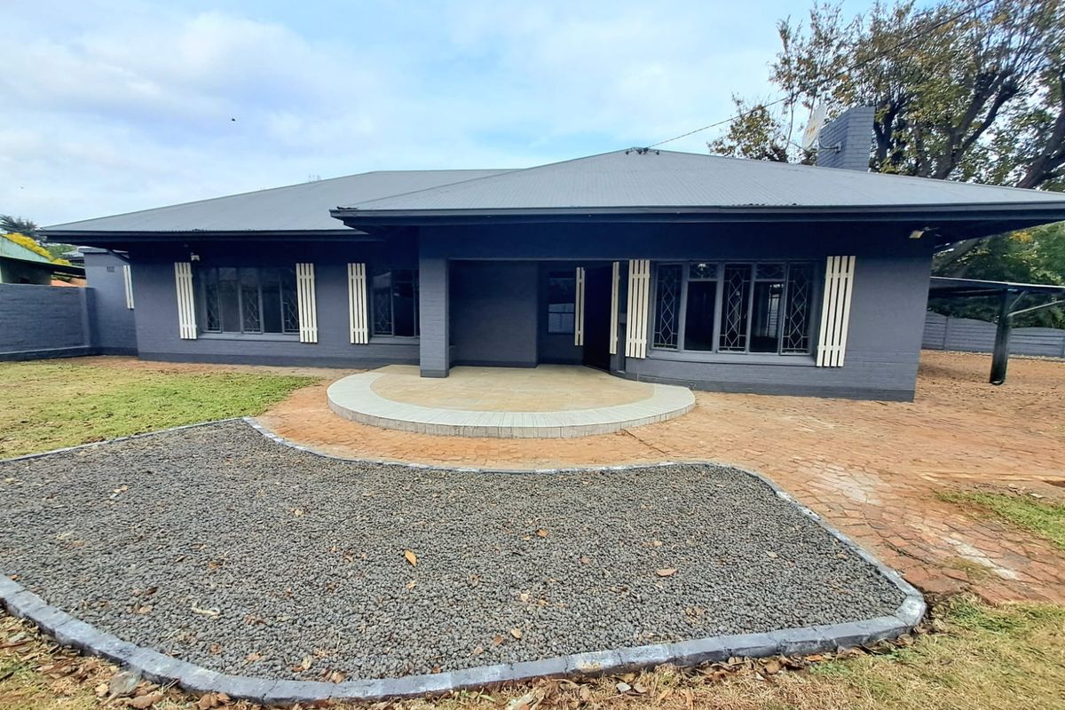Rear view of a single-story house featuring a dark grey painted brick facade, a tiled patio area, and a low-maintenance gravel and paved garden.