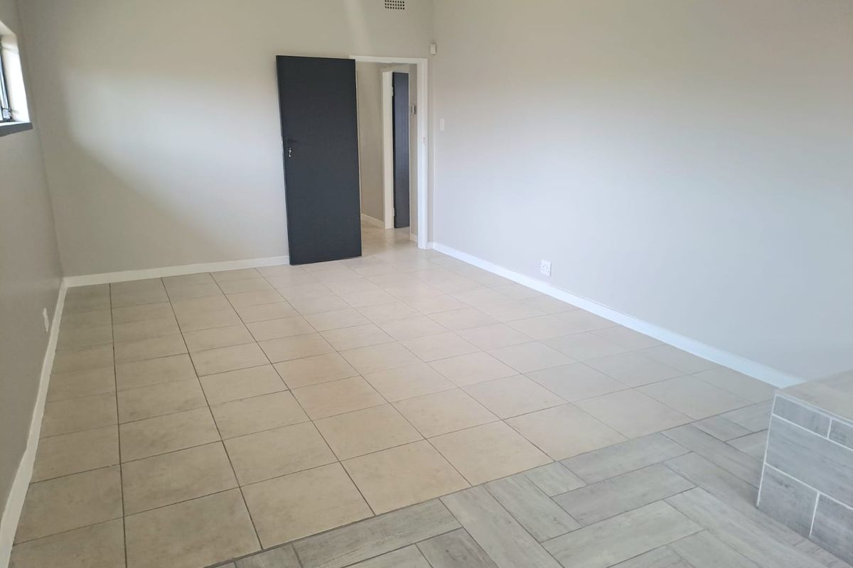 A spacious, empty living area featuring neutral tiled flooring, clean walls, and internal access doors.