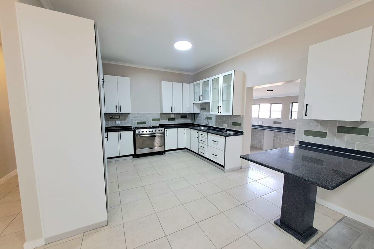 A clean, modern kitchen featuring white cabinetry, dark granite countertops, a gas stove, and a breakfast nook, with neutral tiled flooring throughout.