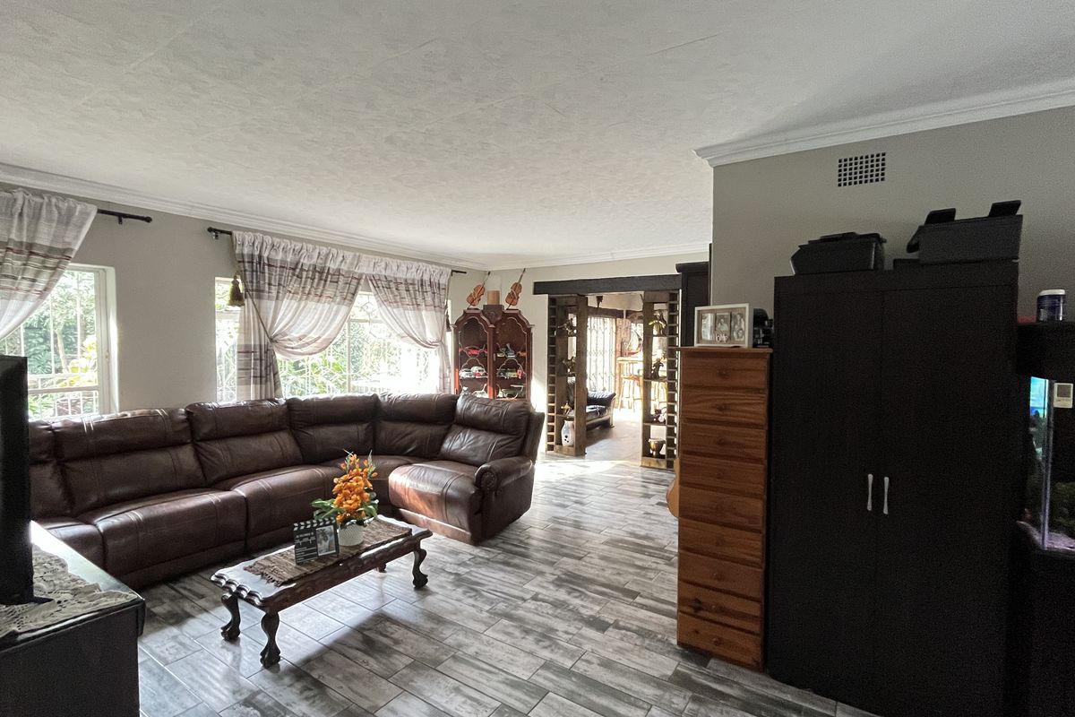 Spacious living area featuring wood-look tiled flooring, crown molding, and an open-plan layout leading to an adjacent room.