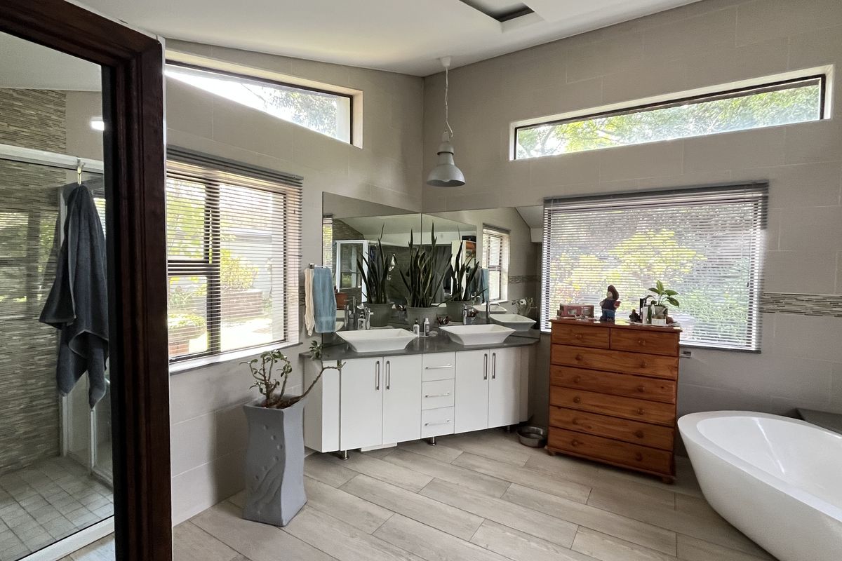 Modern bathroom featuring a double vanity with vessel sinks, a freestanding bathtub, a glass-enclosed shower, and large windows providing ample natural light.