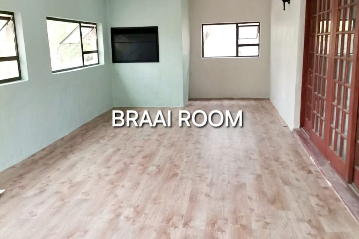 Spacious interior braai room featuring wood-look laminate flooring, recessed ceiling lighting, and large wooden-framed glass doors leading to the exterior.