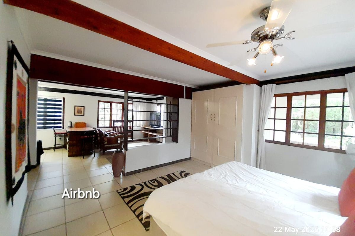 Spacious bedroom featuring exposed timber ceiling beams, built-in cabinetry, and an adjoining living area with tiled flooring throughout.