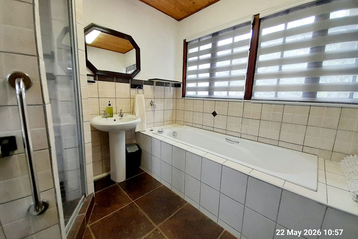 A functional bathroom featuring a built-in bathtub, pedestal basin, and a separate glass-enclosed shower with tiled walls and a timber-paneled ceiling.