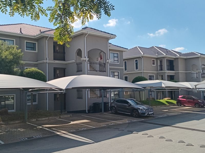 Exterior view of a multi-story townhouse complex featuring covered parking bays, tiled roofing, and private balconies.