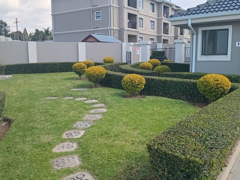 A well-maintained garden area featuring manicured hedges, stone stepping stones, and a paved patio section adjacent to the building structure.