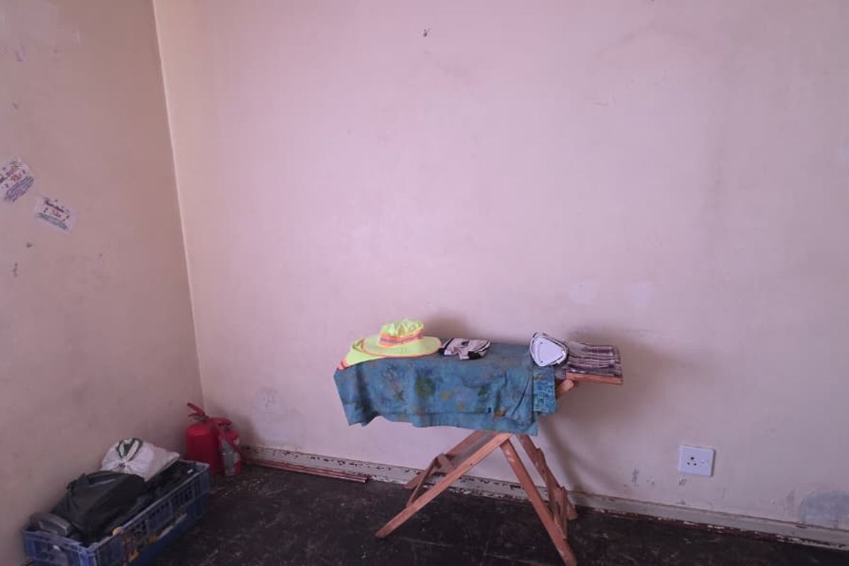 A small, sparsely furnished room featuring plain walls and dark flooring, requiring cosmetic updates and wall repairs.