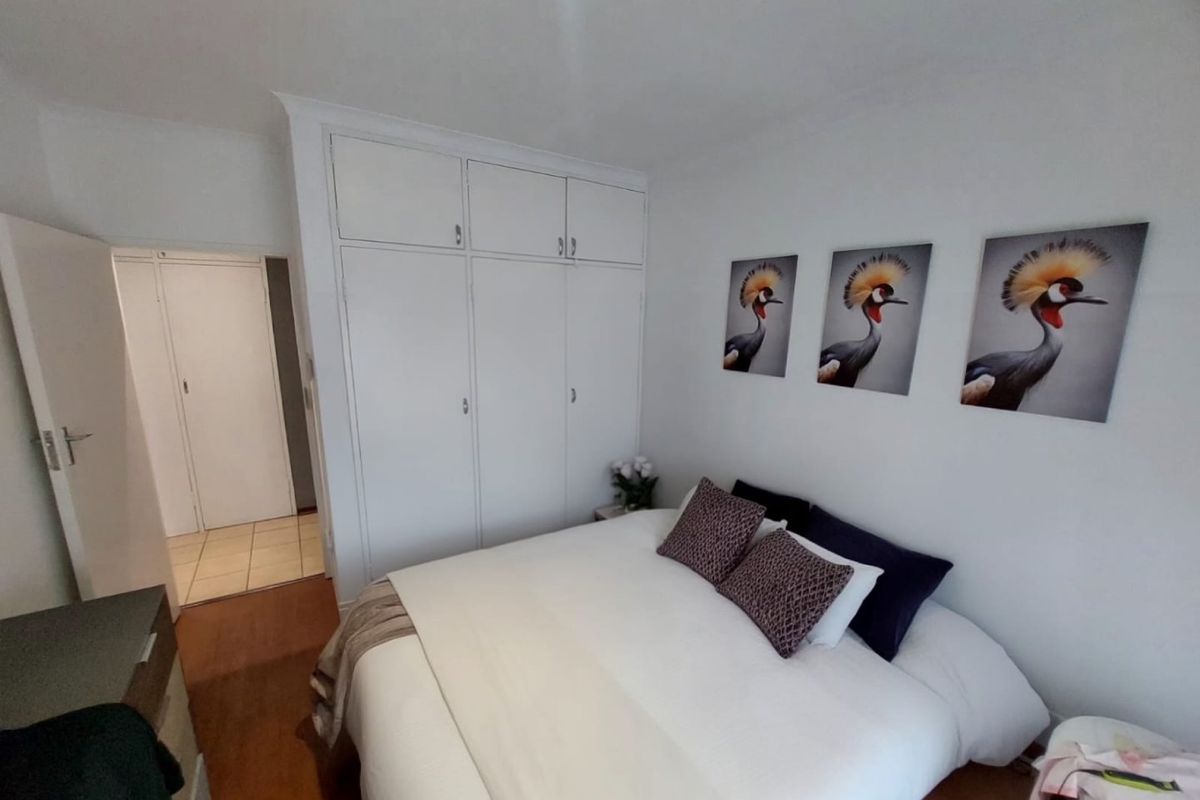 A bedroom featuring built-in cupboards and laminate flooring, with an adjacent hallway visible through the doorway.