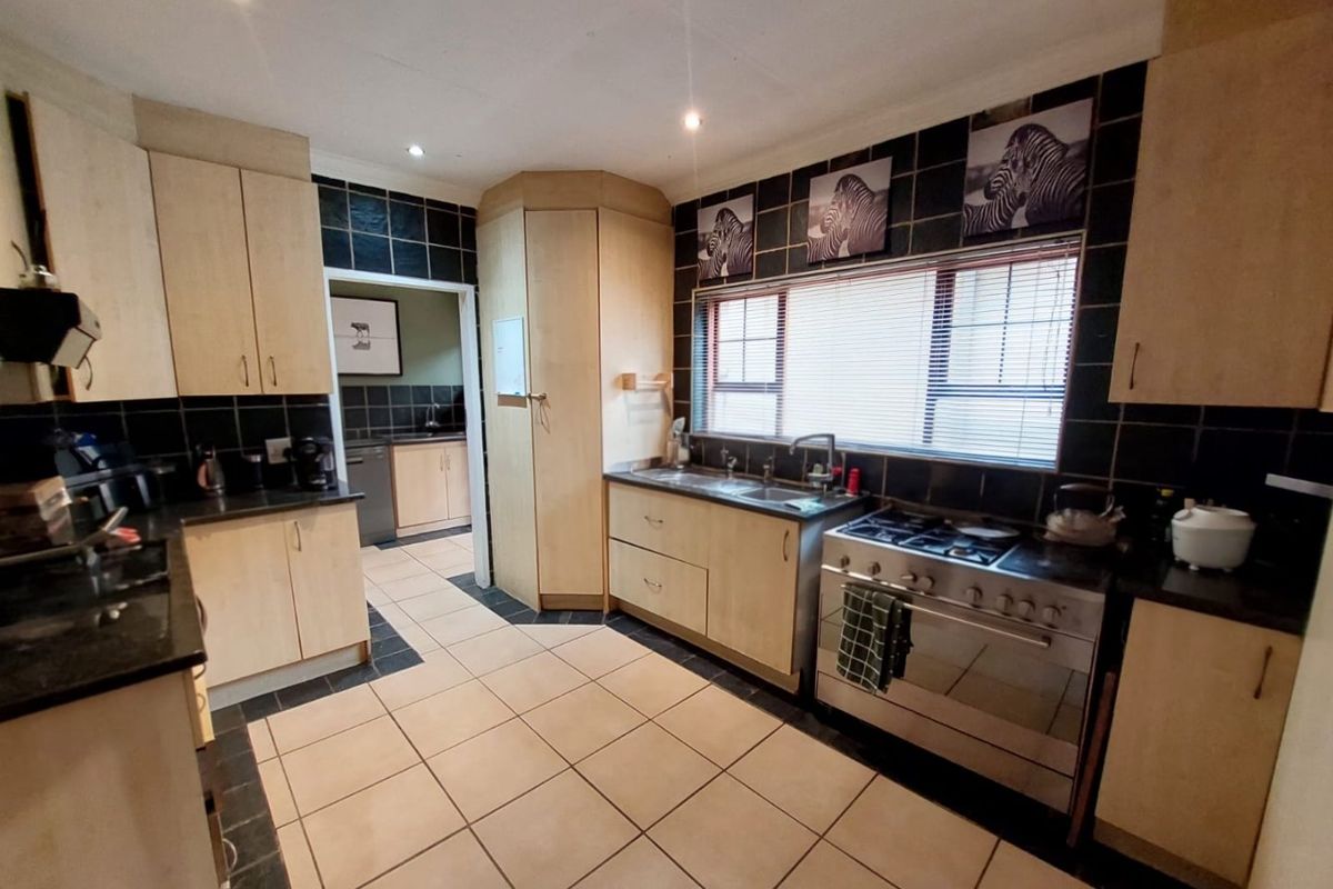 Functional kitchen featuring light wood cabinetry, dark tiled splashbacks, tiled flooring, and a freestanding gas stove with oven.