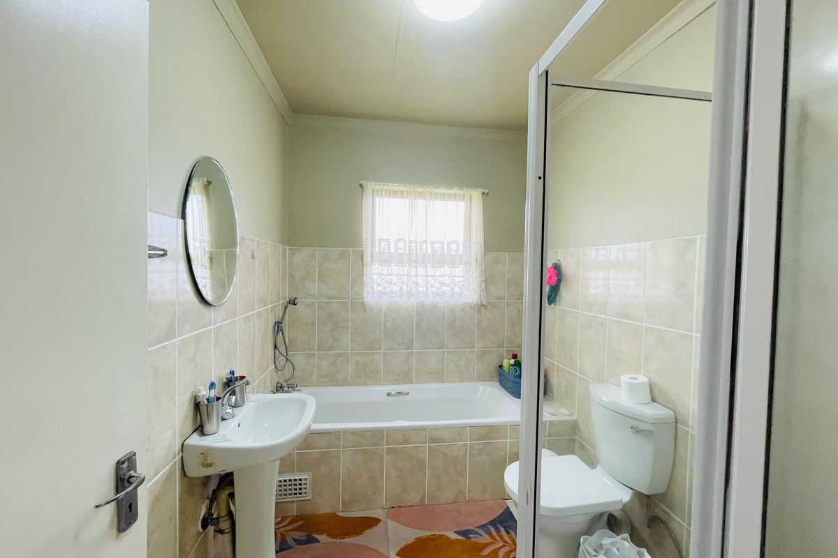 A functional bathroom featuring a pedestal basin, a bathtub with shower attachment, and a toilet, finished with neutral wall tiling.