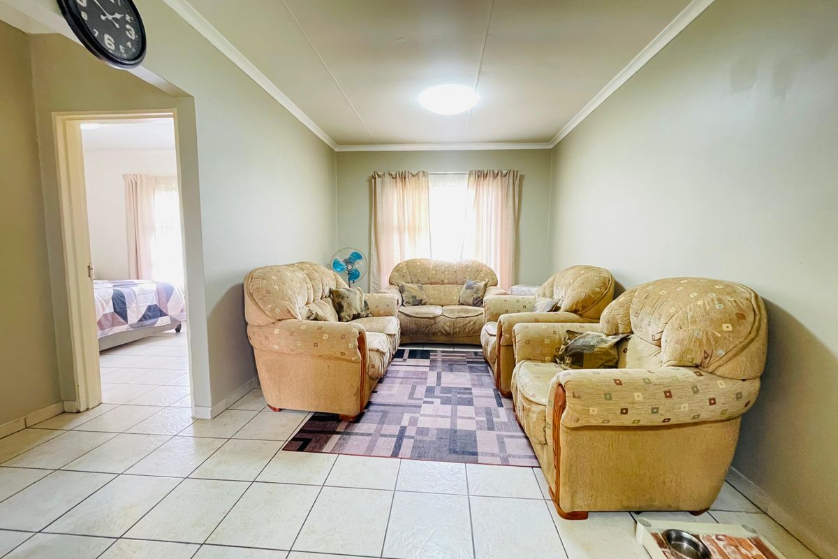 A living room featuring neutral tiled flooring and a doorway leading to an adjacent bedroom.