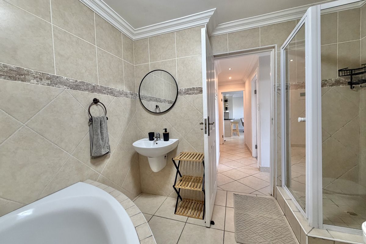 A well-maintained bathroom featuring a tiled shower enclosure, a built-in bathtub, and a pedestal basin with neutral wall tiling.