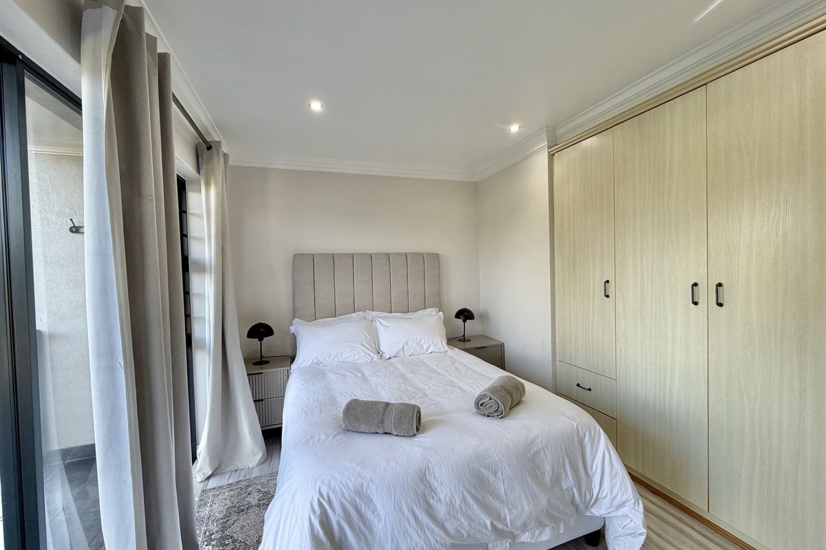 A well-maintained bedroom featuring built-in cupboards, recessed downlighting, and a sliding glass door providing access to an outdoor area.