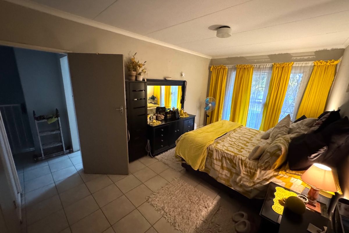 A spacious bedroom featuring tiled flooring, large windows with natural light, and a neutral wall palette.