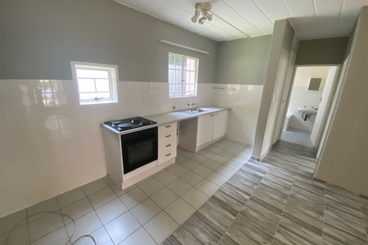 A functional kitchen featuring built-in cabinetry, a stove and oven, and tiled flooring, with an adjacent hallway leading to a bathroom.