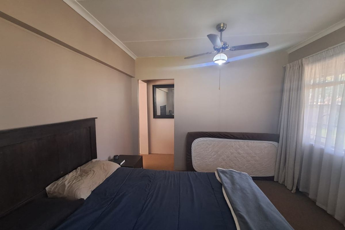 A functional bedroom featuring carpeted flooring, a ceiling fan, and neutral wall tones, offering a comfortable and well-lit sleeping space.