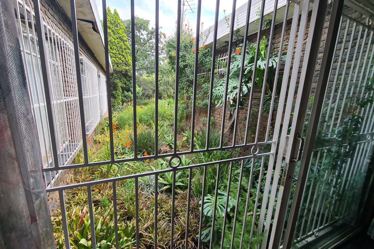 View of a lush, established rear garden area accessed through a sliding glass door protected by a metal security gate.