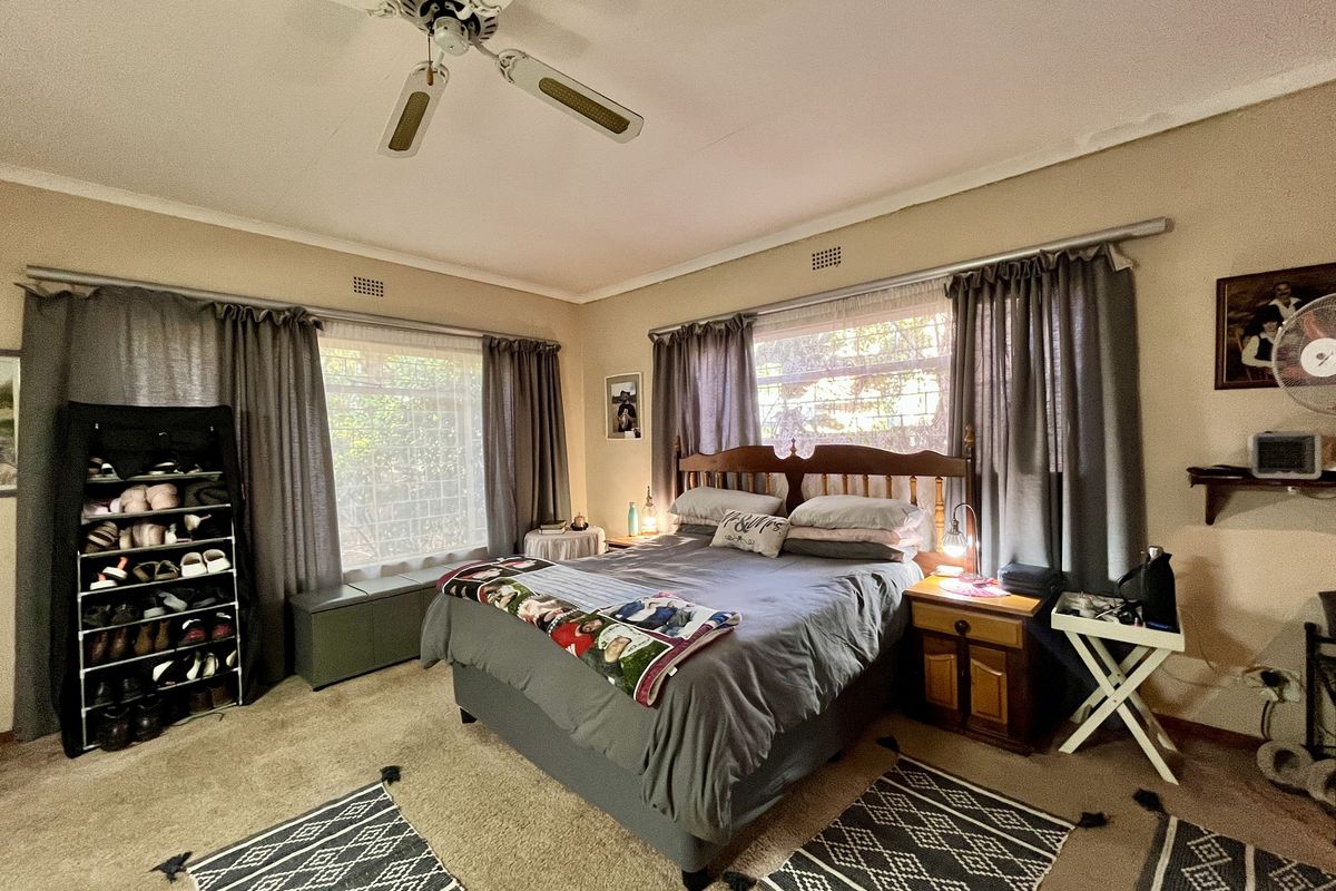 A spacious bedroom featuring large windows with curtain tracks, a ceiling fan, and neutral wall finishes.