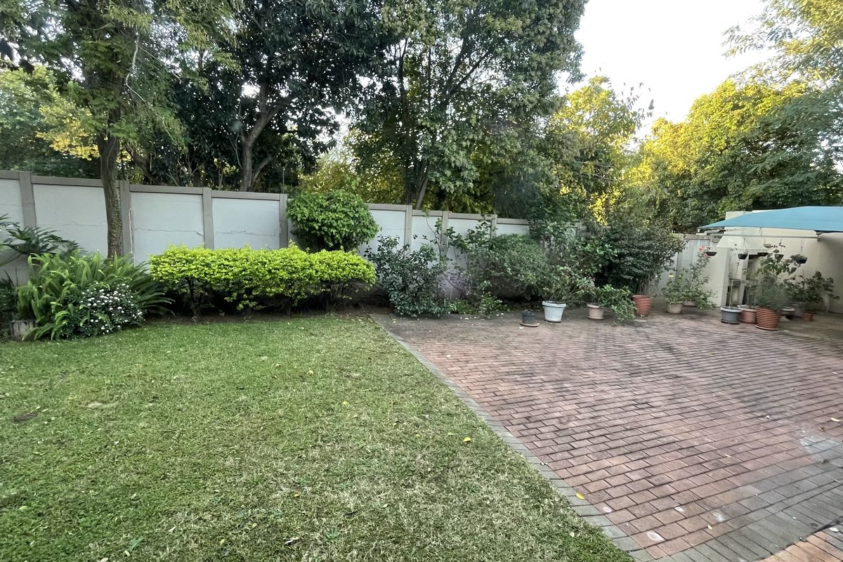 A private rear garden featuring a brick-paved patio area, established lawn, and perimeter boundary wall with mature trees.