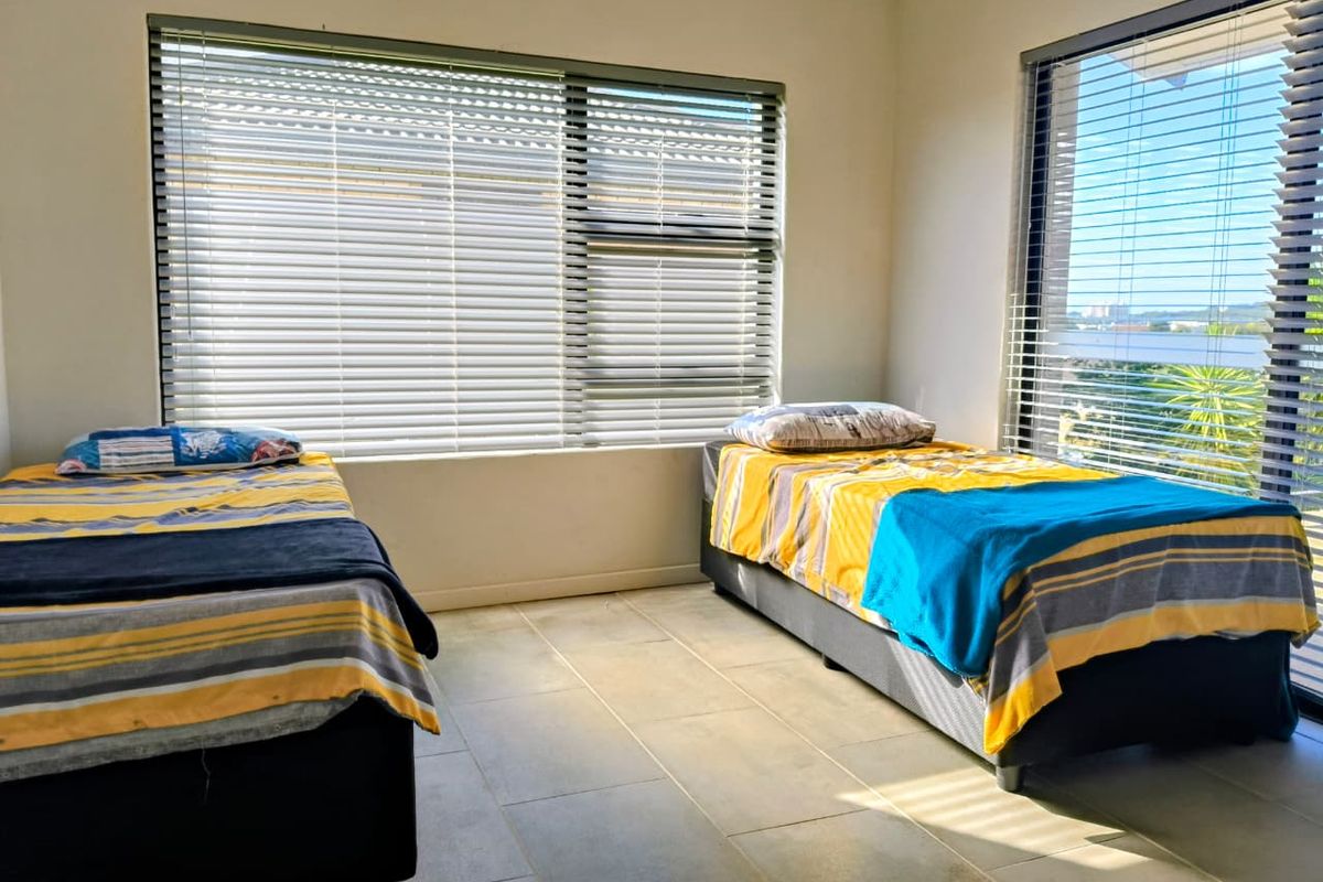 A bright bedroom featuring large windows with fitted horizontal blinds and neutral tiled flooring.