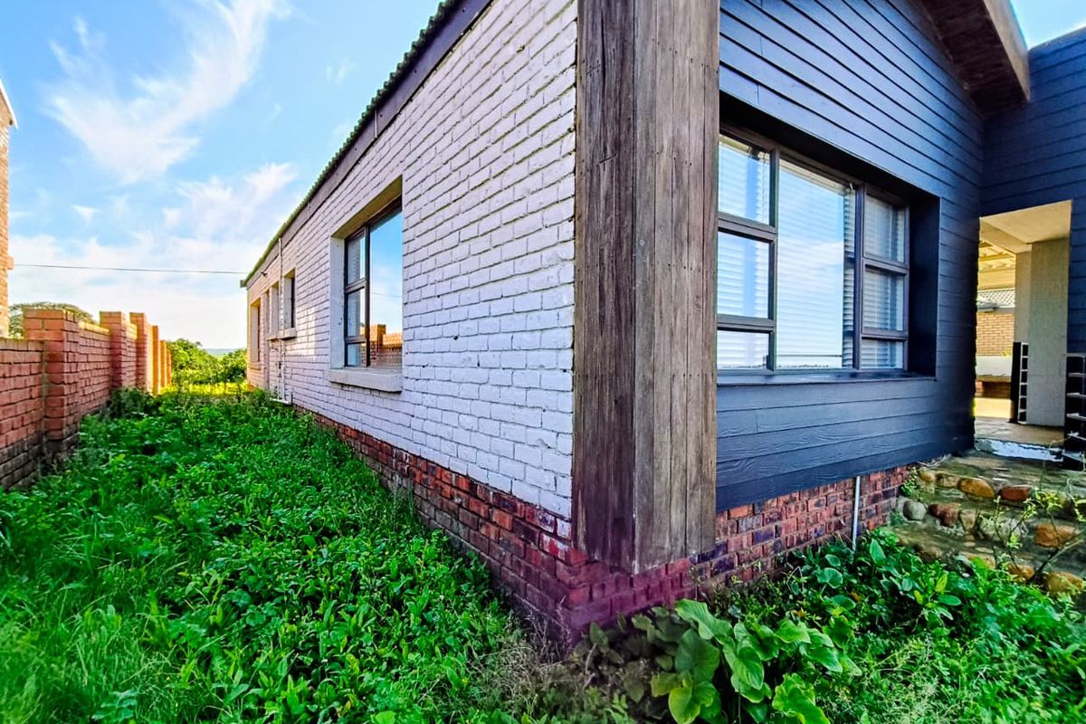Side view of the property featuring a mix of painted brick and dark timber cladding with large windows and an adjacent brick boundary wall.