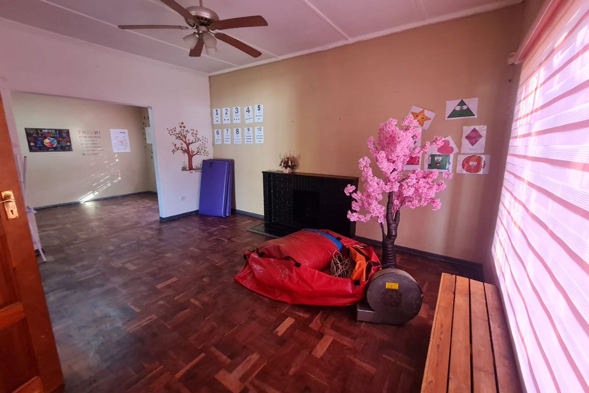 A spacious living area featuring original parquet flooring, a built-in fireplace, and a ceiling fan, with an open-plan layout leading to an adjacent room.