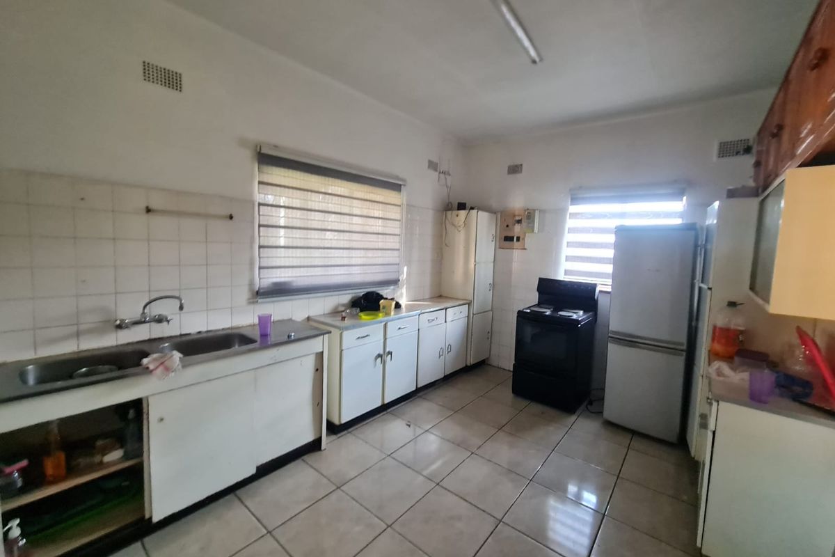 A functional kitchen featuring tiled flooring, built-in cabinetry, a double sink, and space for a freestanding stove and refrigerator.