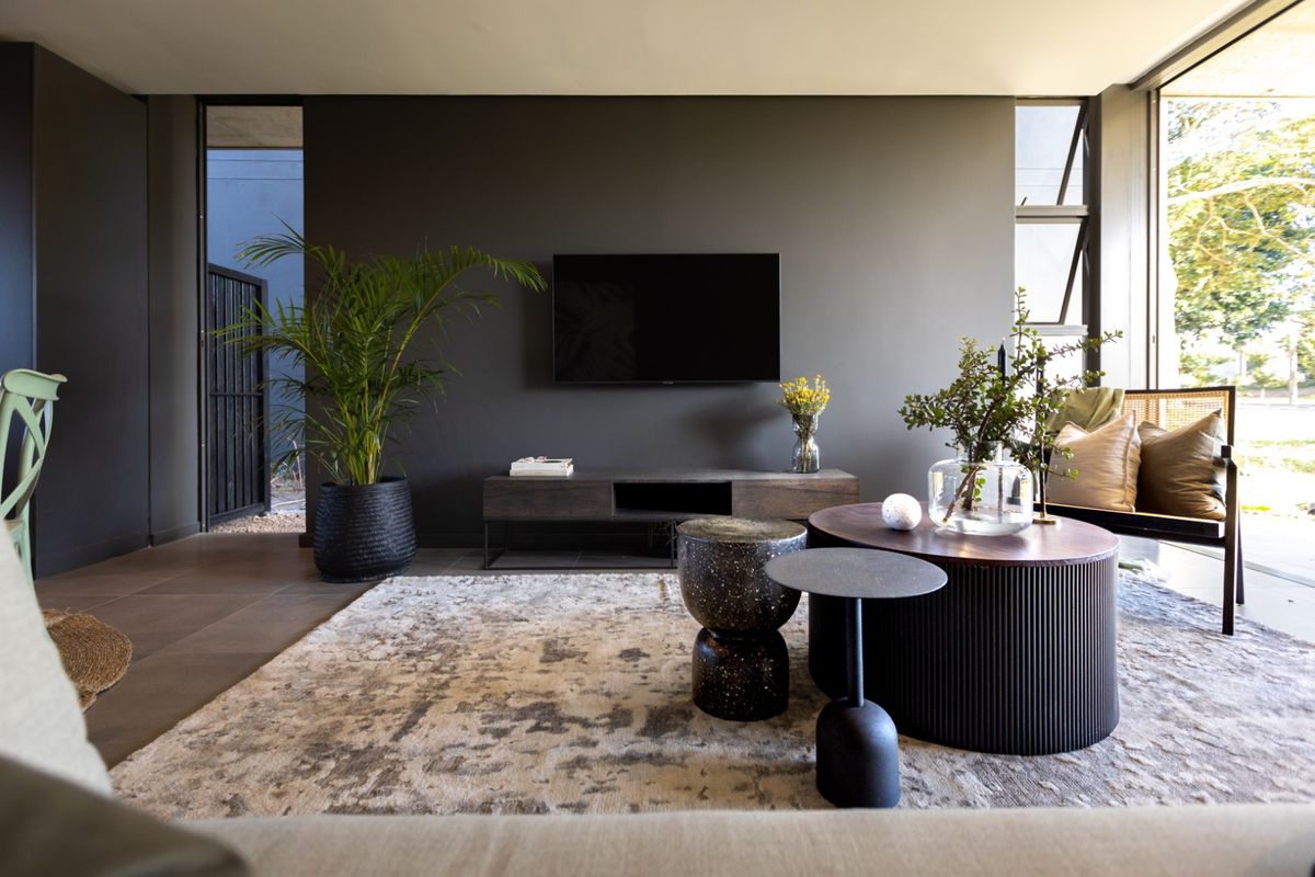 Modern living room featuring dark feature walls, large format floor tiles, and expansive windows providing natural light and garden views.