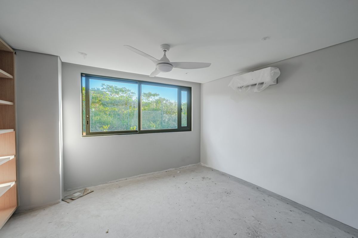 An empty bedroom featuring a ceiling fan, wall-mounted air conditioning unit, and built-in shelving, awaiting final flooring installation.