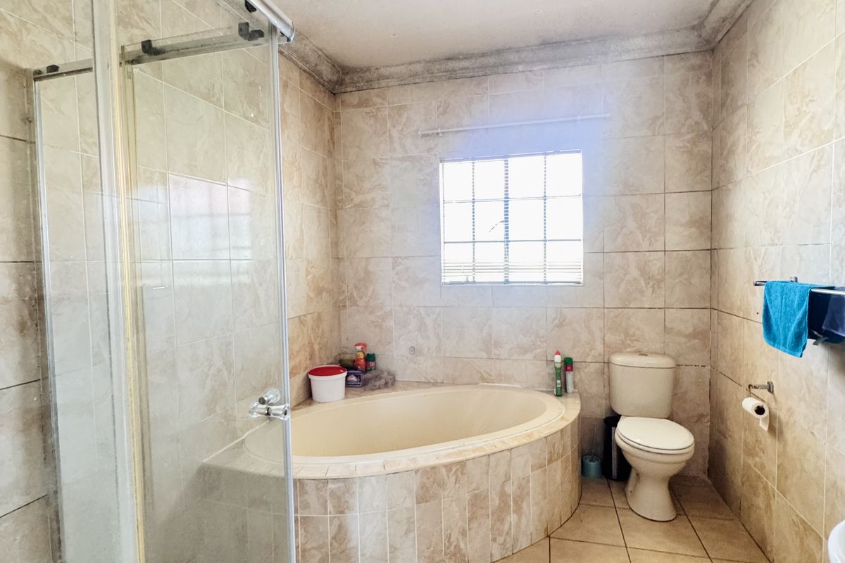 A functional bathroom featuring a built-in corner bathtub, a separate glass-enclosed shower, and tiled flooring and walls throughout.