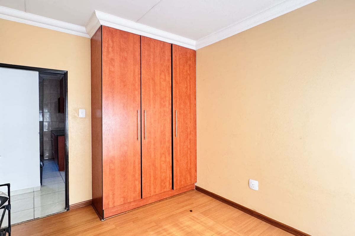 A bright, empty bedroom featuring built-in wooden cabinetry, laminate flooring, and crown molding, with an adjacent doorway leading to another room.