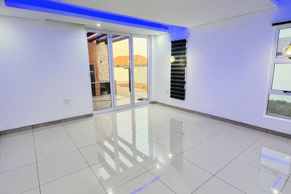 Spacious, modern living area featuring high-gloss tiled flooring, a contemporary recessed ceiling with integrated blue LED lighting, and large sliding doors to the patio.