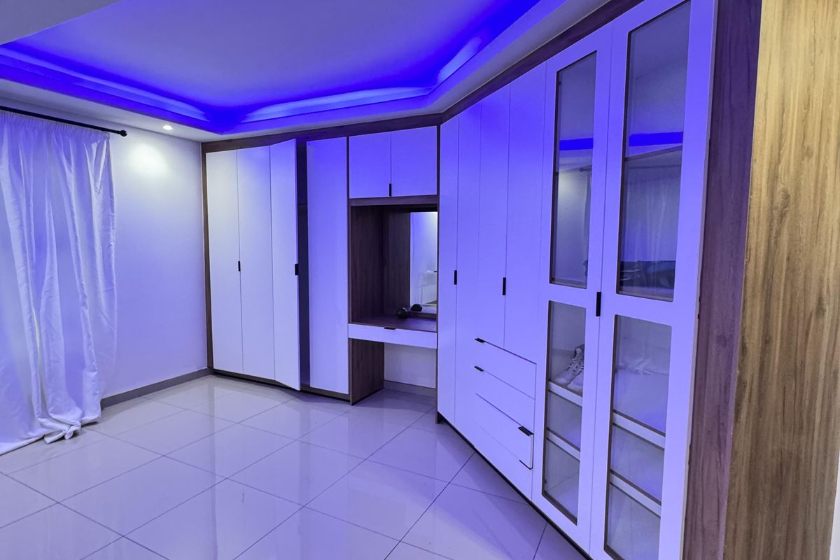 Modern bedroom featuring extensive built-in cabinetry with integrated vanity, polished tile flooring, and ambient recessed ceiling lighting.