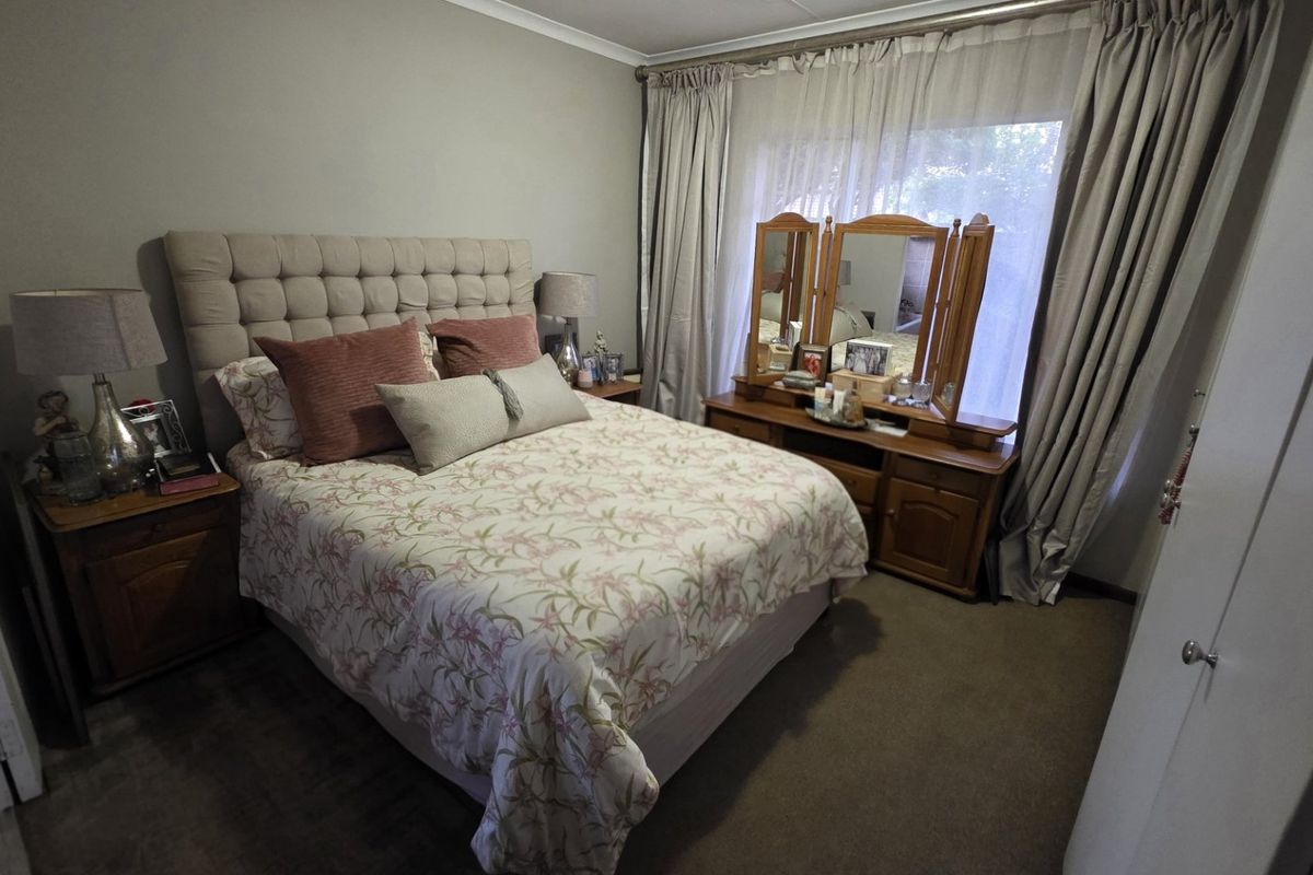 A well-proportioned bedroom featuring neutral wall tones, carpeted flooring, and large windows with floor-to-ceiling curtains, providing a comfortable and functional living space.